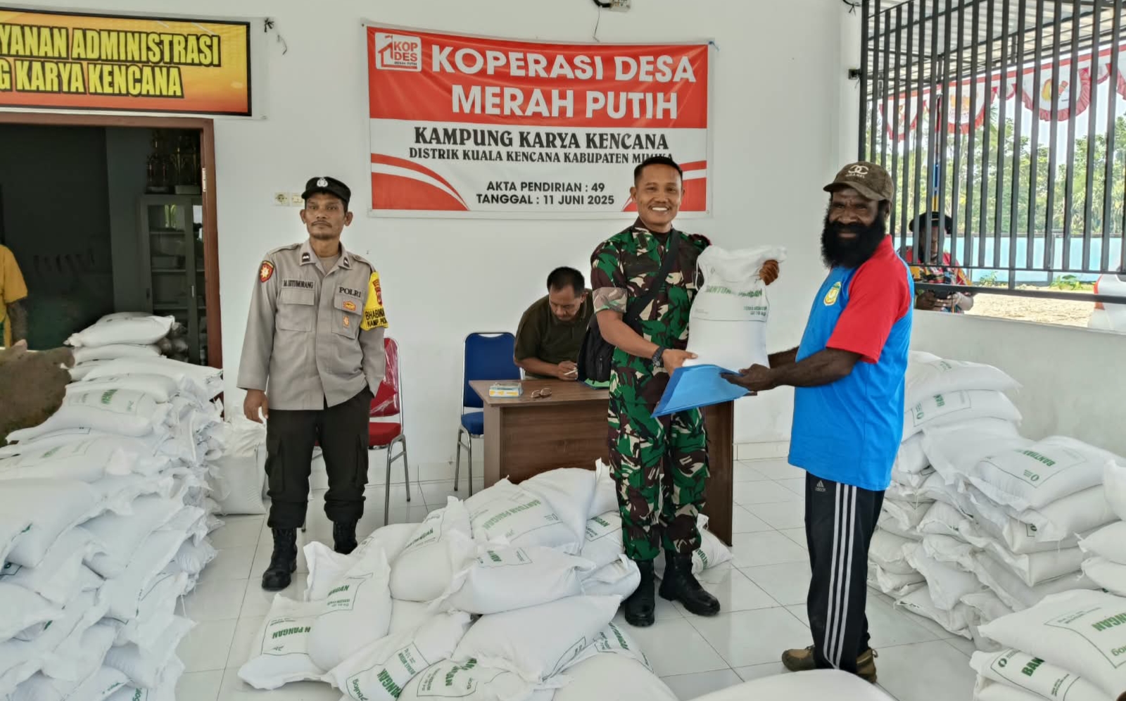 Babinsa Koramil Kuala Kencana menyerahkan bantuan beras kepada warga disaksikan oleh Kepala Kampung Karya Kencana, Rakam Suntoro, Bhabinkamtibmas Kampung Karya Kencana dan warga yang hadir 