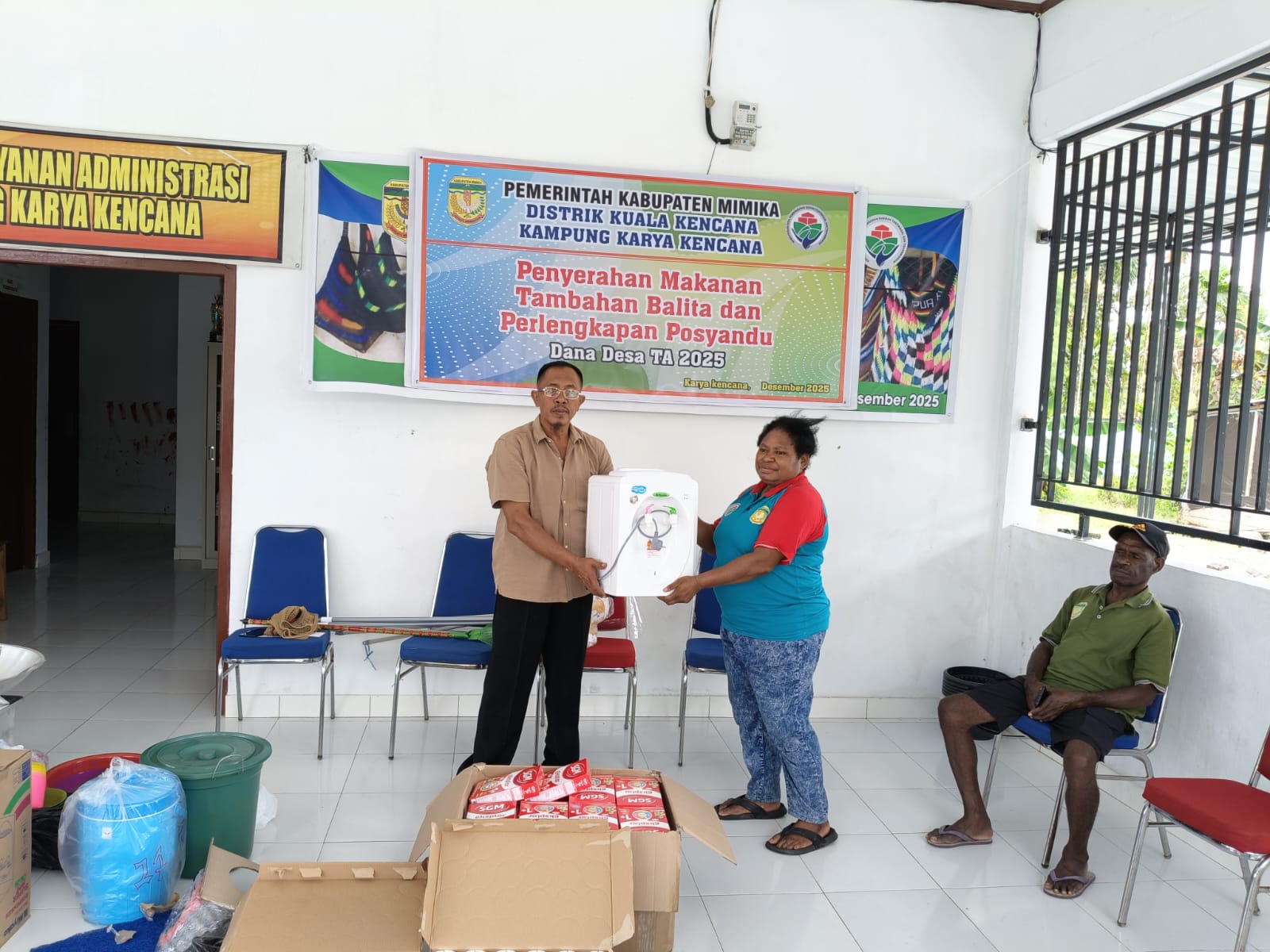 Kepala Kampung Karya Kencana Rakam Suntoro saat menyerahkan dispenser kepada salah satunya kader posyandu 