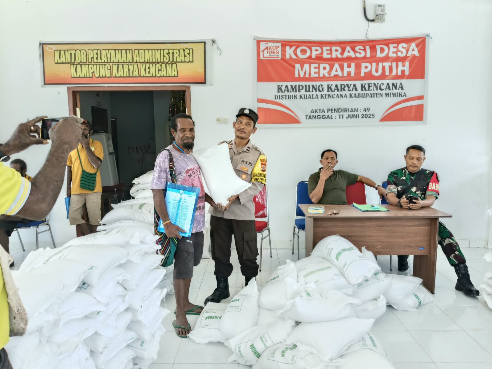 Bhabinkamtibmas Kampung Karya Kencana menyerahkan bantuan beras kepada warga disaksikan oleh Kepala Kampung Karya Kencana, Rakam Suntoro, Babinsa Koramil Kuala Kencana dan warga yang hadir 