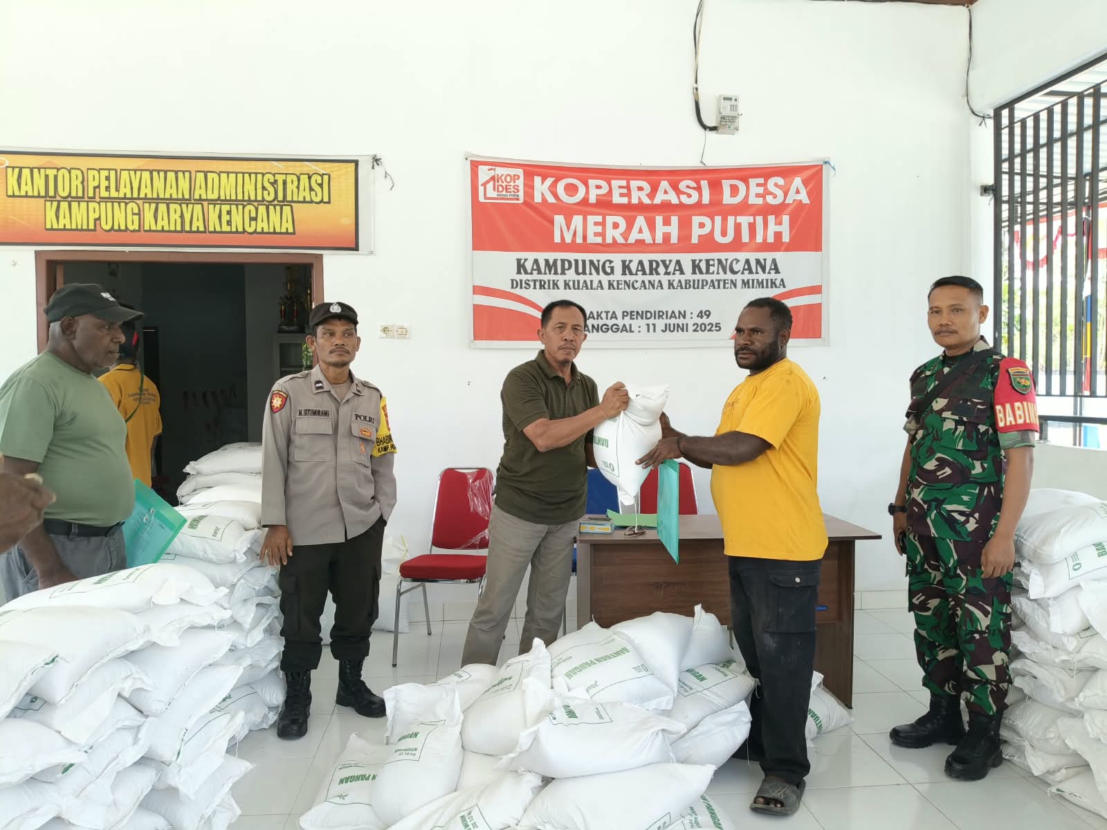 Kepala Kampung Karya Kencana, Rakam Suntoro menyerahkan bantuan beras kepada warga disaksikan oleh Babinsa Koramil Kuala Kencana, Bhabinkamtibmas Kampung Karya Kencana dan warga yang hadir 