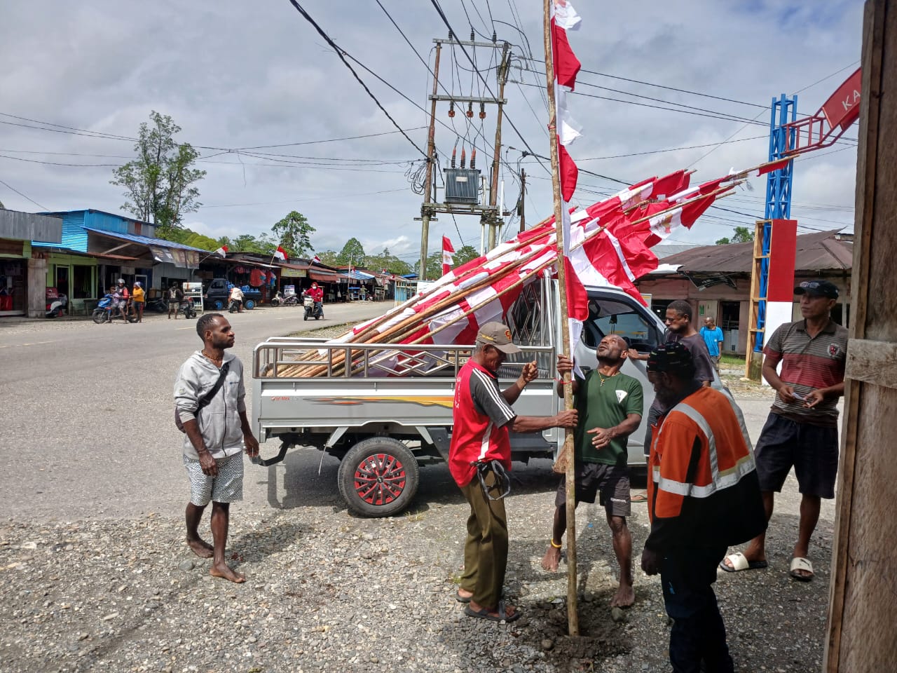 Warga sedang menancapkan tiang bendera di pinggir jalan di Kampung Bhintuka