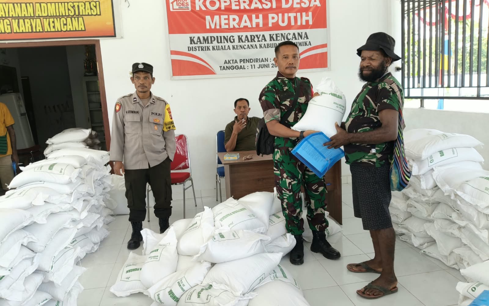 Babinsa Koramil Kuala Kencana menyerahkan bantuan beras kepada warga disaksikan oleh Kepala Kampung Karya Kencana, Rakam Suntoro, Bhabinkamtibmas Kampung Karya Kencana dan warga yang hadir 