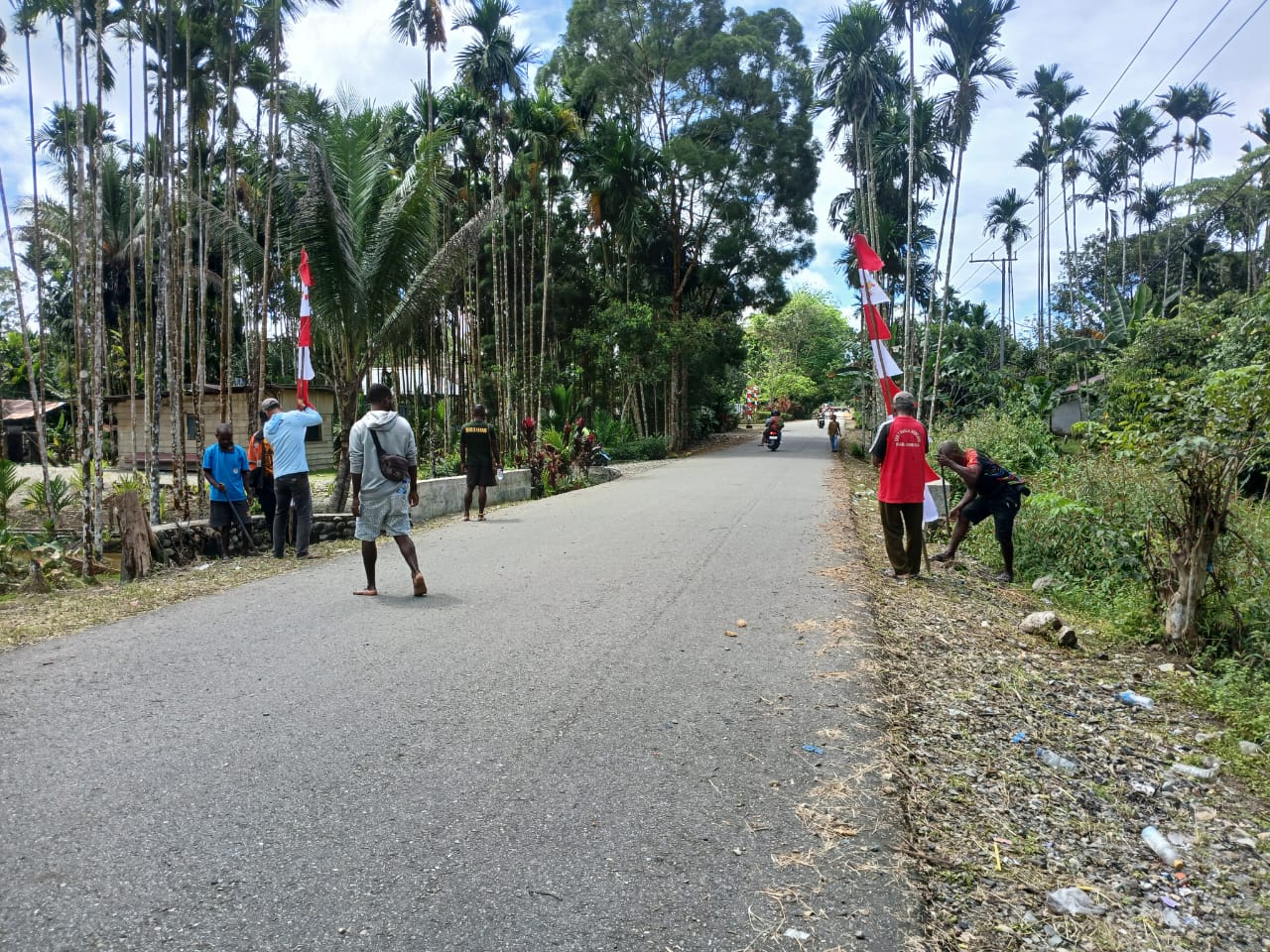 Warga sedang menancapkan tiang bendera di pinggir jalan di Kampung Bhintuka