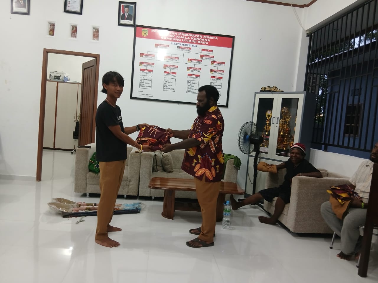 Kepala Kampung Utikini I saat menyerahkan kemeja kepada warganya